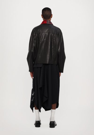 Black leather jacket with a red and plaid collar, worn over a draped black skirt. Accents include silver safety pins and white socks.