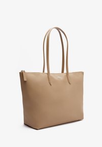Sac tote beige en matériau synthétique texturé. Il possède deux longues poignées et une fermeture éclair. Détail logo discret à l'avant.