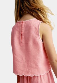 Top sans manches rose avec un ourlet festonné, présentant une texture de tissu et une fermeture par bouton à l'arrière. Design simple, matériau doux et couture neutre.