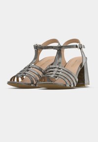 Pelēkas metāliskas sandales ar siksnām, atvērtām purngalām, biezu blokpapēdi un regulējamām potīšu siksnām. Sintētisks materiāls.