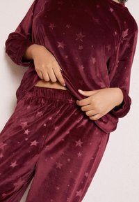 Set de loungewear din catifea bordeaux, cu motive de stele; prezintă mâneci lungi și talie elastică. Textură moale și croială lejeră.