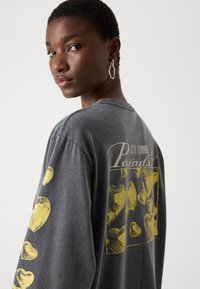 Gray oversized sweatshirt featuring a yellow heart pattern on the sleeves and back, with "City Summer Paradise" text in a stylized font.