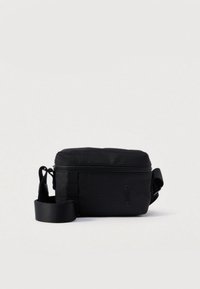 Συμπαγής μαύρη τσάντα χιαστί με κλείσιμο φερμουάρ, ρυθμιζόμενος ιμάντας και το λογότυπο "HUGO" τυπωμένο μπροστά σε απλό φόντο.