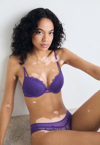 Lila Spitzen-BH mit geometrischem Muster und gewellten Kanten, kombiniert mit passendem, transparentem Bikini-Brief, beide mit verstellbaren Trägern.