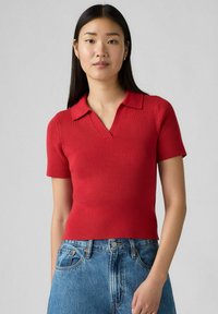 Röd randig polotröja med kort ärm och djup V-ringning, tillsammans med högmidjade denimshorts. Slät textur, åtsittande form.