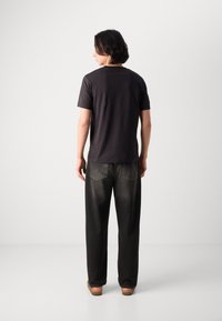 T-shirt nera in cotone con scollatura rotonda, abbinata a jeans larghi grigio scuro con tasche posteriori e cuciture visibili. Design semplice e casual.