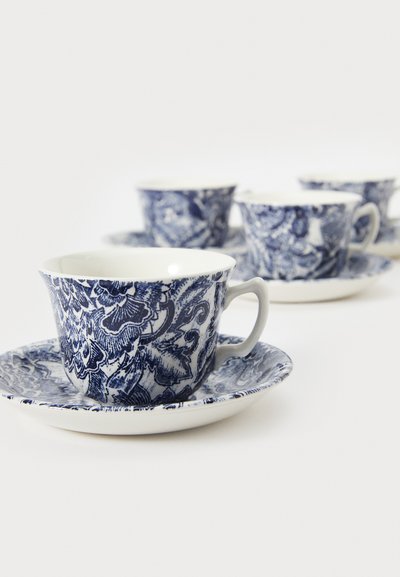 Chávena de porcelana azul e branca com padrões florais, borda curva e pega; acompanhada por um pires combinando com design semelhante.