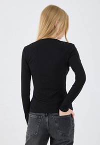 Svart randig långärmad topp med en åtsittande silhuett, rund hals och slät textur, i kombination med högmidjade mörkgrå jeans med fickdetaljer.