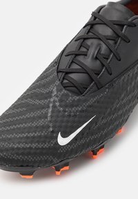 Black soccer cleat with a textured upper featuring a diamond pattern. White Nike logo, black laces, and orange studs on the sole.