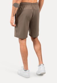 Braune Sportshorts mit einem elastischen Bund, seitlichen Taschen und einer glatten Textur, getragen mit weißen Turnschuhen.
