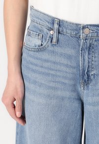 Jeans in denim azzurro chiaro con vita alta, dotati di chiusura con bottone, cinque tasche e una leggera sfumatura nella texture del tessuto.