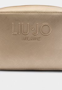 Bežinis tekstūruotas audinio maišelis su raižytu „LIU·JO MILANO“ logotipu priekyje ir užtrauktuku viršuje.