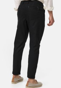 Sorte bukser med slim fit, der har baglommer og opsmøgede ben. Bæres med lysfarvede espadrillos.