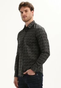 Camisa de manga larga negra y con patrón, de corte ajustado, que presenta un collar con botones y sutiles diseños geométricos.