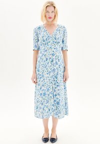 Robe midi à imprimé floral en bleu clair et blanc, avec un col en V, des manches courtes et une silhouette fluide. Associée à des chaussures plates marine.