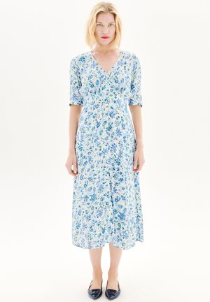 Abito midi a stampa floreale in azzurro chiaro e bianco, con scollo a V, maniche corte e una silhouette fluida. Abbinato a scarpe piatte blu navy.