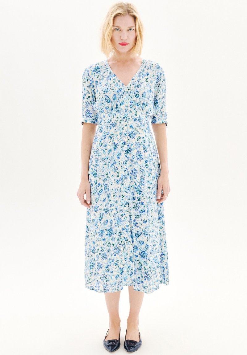 Robe midi à imprimé floral en bleu clair et blanc, avec un col en V, des manches courtes et une silhouette fluide. Associée à des chaussures plates marine.