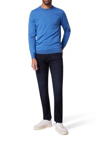 Blauer Strickpullover mit Rundhalsausschnitt, kombiniert mit dunklen Jeans und weißen Sneakern. Lässiges Design mit glatter Textur und minimalem Markendetail.