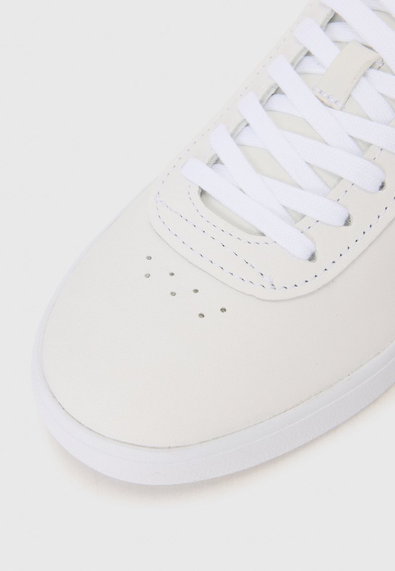 Baskets blanches avec un dessus en cuir lisse, un bout perforé, des lacets blancs plats et une semelle en caoutchouc blanc texturé.