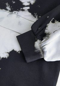 Fekete-fehér batikolt pulóver anyag, bordás mandzsettákkal, sima felülettel és kontrasztos mintákkal. Közeli nézet a részletekről.