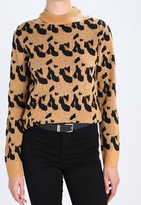Tijgerprint trui in bruin en zwart, gemaakt van gebreide stof. Heeft een geribbelde halslijn en lange mouwen, gecombineerd met zwarte broeken.