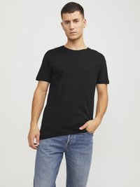Sorte bomulds t-shirt med rund hals og korte ærmer, parret med lyseblå denim jeans. Modellen står med den ene hånd i lommen.