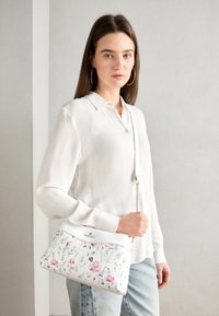 Kwiatowa torebka z białą podstawą, zdobiona różowymi i zielonymi wzorami roślinnymi. Wykonana z gładkiego materiału, uzupełniona o łańcuszkowy pasek.