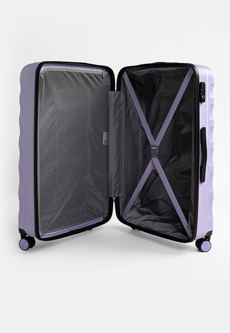 Valise rigide de couleur violet clair, zippée avec un intérieur en maille et des sangles, équipée de quatre roues et d'une bordure noire pour plus de stabilité.
