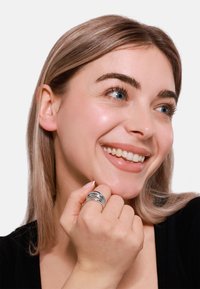 Sterling-Silber Mehrbandring mit polierter Oberfläche, bestehend aus fünf ineinander verschlungenen Ringen. Die Benutzerin lächelt und hält den Ring.