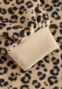 Leopardprint fleece stof med en blød tekstur; har en beige ribbenmanchet i enden af ærmet. Sorte og brunlige pletter over det hele.