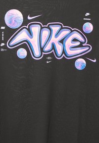 Logo Nike en style graffiti audacieux avec un dégradé pastel, entouré de ballons de basket et de plusieurs petits logos Nike swoosh sur fond noir.
