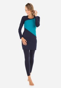 Långärmad tunika i marinblått med en teal-diagonalpanel, tillsammans med matchande leggings. Mjuk tyg, figurnära design, minimalistiska accenter.