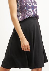 Jupe évasée noire en tissu léger, présentant une texture lisse et une taille mi-haute, portée avec un haut à motifs.