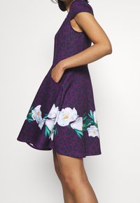 Lila klänning med leopardtryck och blommönster, med korta ärmar, en svängd kjol och sidofickor. Slät tygkvalitet.