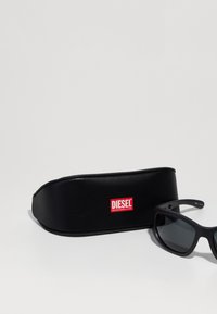 Mustad prillid tumedate objektiividega, mattviimistlusega ja punase Diesel logo'ga mustal karbil. Karbi sisemus on polsterdatud ja kõver.