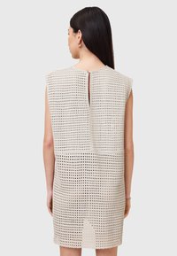 Kortærmet kjole i et lyst beige perforeret stof, med en nøglehul detalje bagpå og en lige pasform, samt en let asymmetrisk kant.