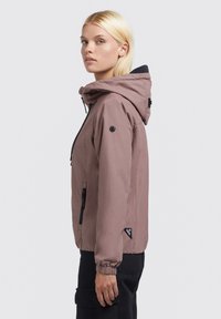Helle rosa Kapuzenjacke aus weichem Material. Verfügt über schwarze Reißverschlusstaschen, elastische Bündchen und ein Logo-Patch am Arm.