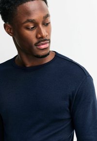 Navy blue long-sleeve shirt in a ribbed texture with a round neckline and subtle shoulder seams, made from soft, knit material.