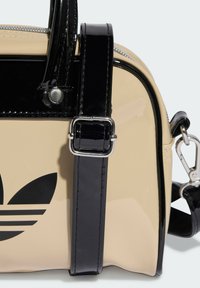 Beige patent handbag with black glossy accents, featuring a silver buckle on a strap and a prominent black logo design on the front.