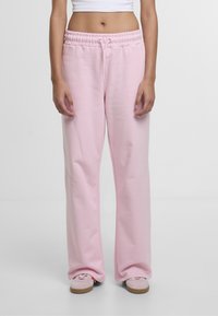 Lyserøde sweatpants med snor i taljen, brede ben og en glat stoffasthed. Kombinationen med pink sneakers med en brun sål.