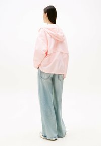 Giacca a cappuccio rosa con vestibilità rilassata, caratterizzata da uno stile corto, realizzata in materiale leggero. Abbinata a jeans larghi di un azzurro chiaro.