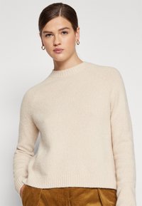 Helles beige Wollpullover mit rippenförmigem Halsausschnitt und Saum. Verfügt über lange Ärmel und eine lockere Passform, die sich gut zum Schichten eignet.
