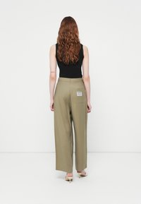 Bredde bukser i olivengrønn farge laget av lett stoff. Har en baklomme med etikett og en ren linning. Kombinert med et svart tanktop.