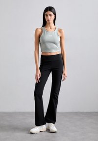Light green cropped tank top with logo, black fitted pants, and white sneakers. Smooth fabric, simple design, and flared pant legs.