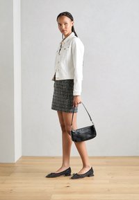 Chaqueta de mezclilla blanca, falda mini a rayas en blanco y negro, bolso negro con estampado de cocodrilo y planos negros con tachuelas y detalle de lazo. Fondo de suelo de madera.