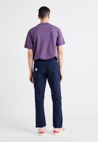 Purple cotton short-sleeve t-shirt paired with navy pants and pink Nike sneakers. Features a logo patch on the pants' back pocket.