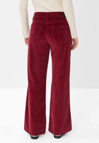 Rote Cordhosen mit weitem Bein und texturiertem Finish, versehen mit Gesäßtaschen und hoher Taille. Der Schnitt reicht bis zu den Knöcheln und hat ein weites Bein.