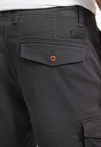 Tamno sive cargo kratke hlače od pamuka s teksturiranim završetkom. Imaju stražnji džep s kopčanjem na gumb i diskretan detalj s logotipom.