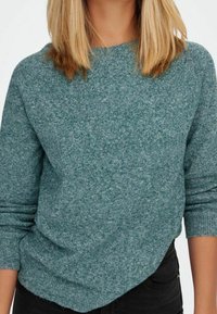 Türkis gestrickter Pullover mit einem Rundhalsausschnitt und langen Ärmeln, der eine weiche Textur und einen leicht lässigen Schnitt aufweist.