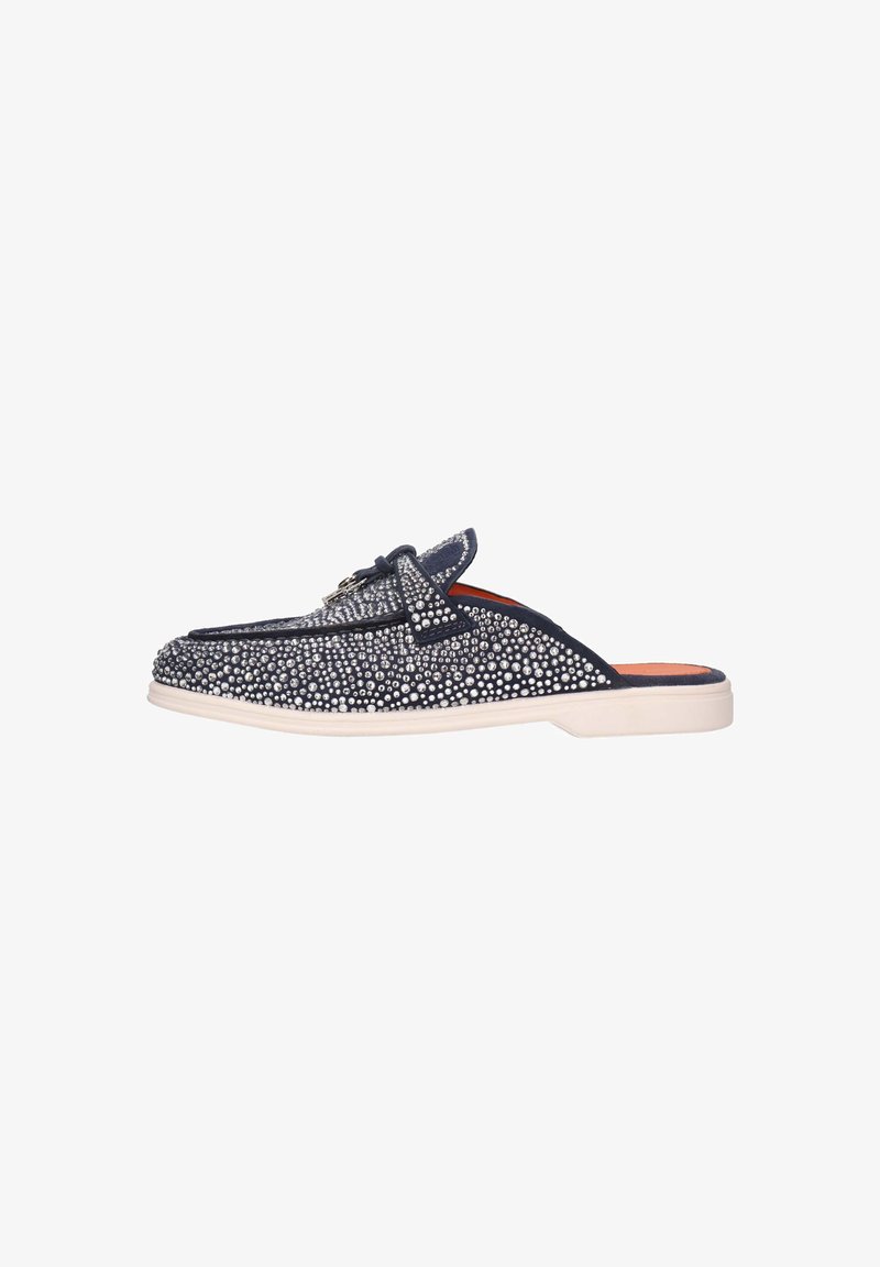Zapatos de tela azul marino sin cordones adornados con tachuelas plateadas, con puntera redonda, suela blanca plana y un detalle de lazo decorativo en la parte superior.